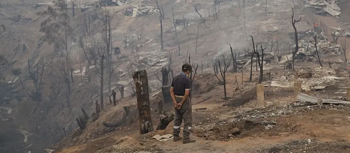 A resident stands in front of homes destroyed by wildfires in the town of Santa Olga in Constitucion, Chile, on Friday, Jan. 27, 2017. Photo: Cristobal Olivares/Bloomberg via Getty Images